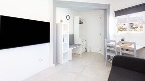 Una habitación moderna y bien iluminada con televisión de pantalla plana, un escritorio con silla, una estantería y una ventana con vistas.