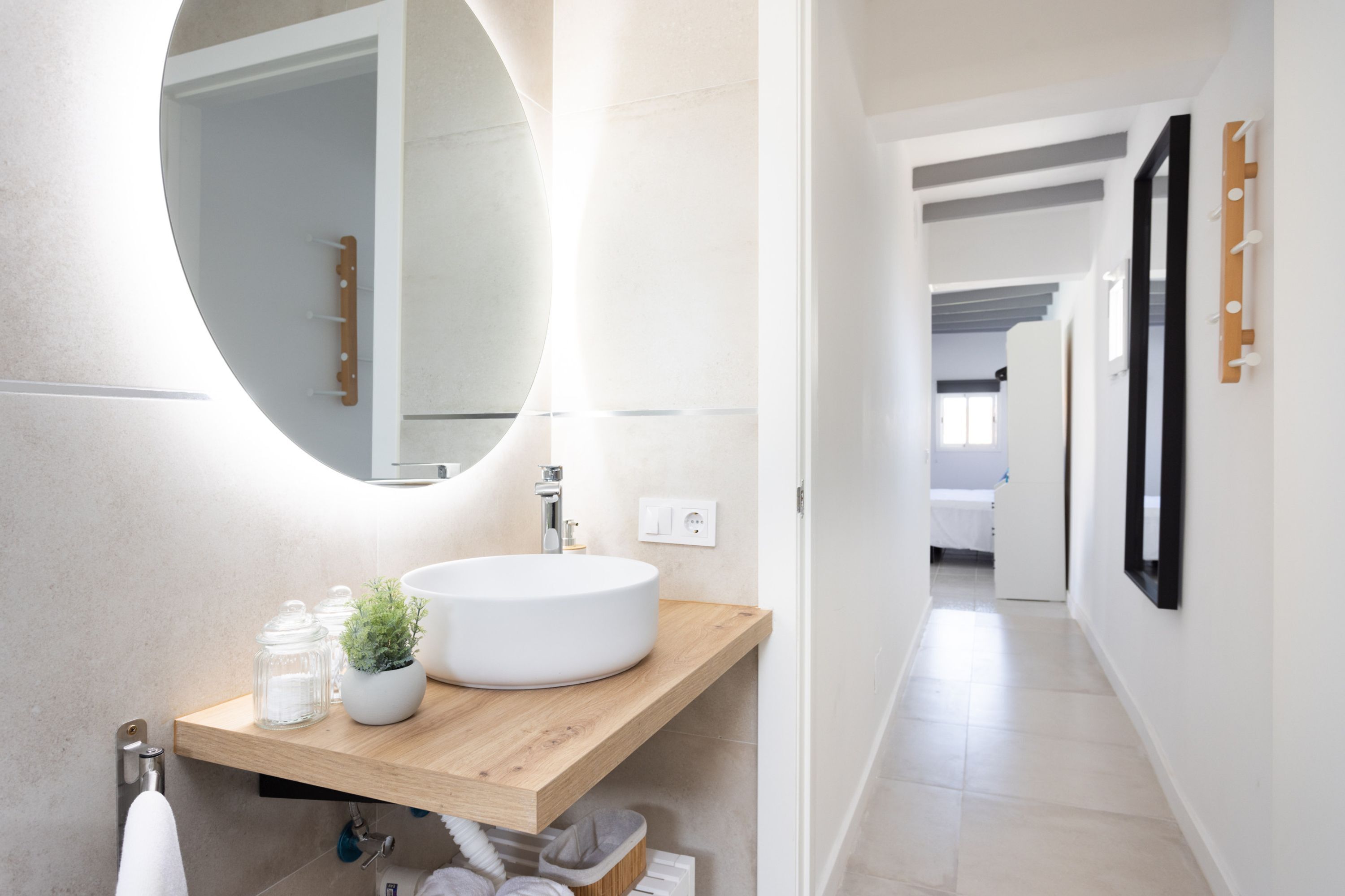 Une salle de bain moderne avec un grand miroir rond, un meuble-lavabo en bois et un lavabo blanc.