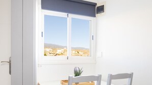 Una habitación con ventana, escritorio, dos sillas y una planta pequeña.