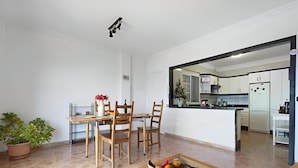 Een moderne woonkamer met een eethoek, een keuken zichtbaar door een open doorgang, en een kamerplant.