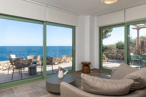A modern living room with a large sliding glass door leading to an outdoor seating area with a view of the sea. - Evilia Beach Villa in Varvara (Zakynthos)