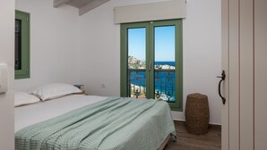 A bedroom with a bed, a window with a view of the sea, and a small round wicker stool. - Evilia Beach Villa in Varvara (Zakynthos)