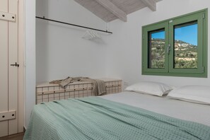 Una camera da letto con un letto, una finestra vista su una collina, un lampadario e una panca di legno con una coperta.