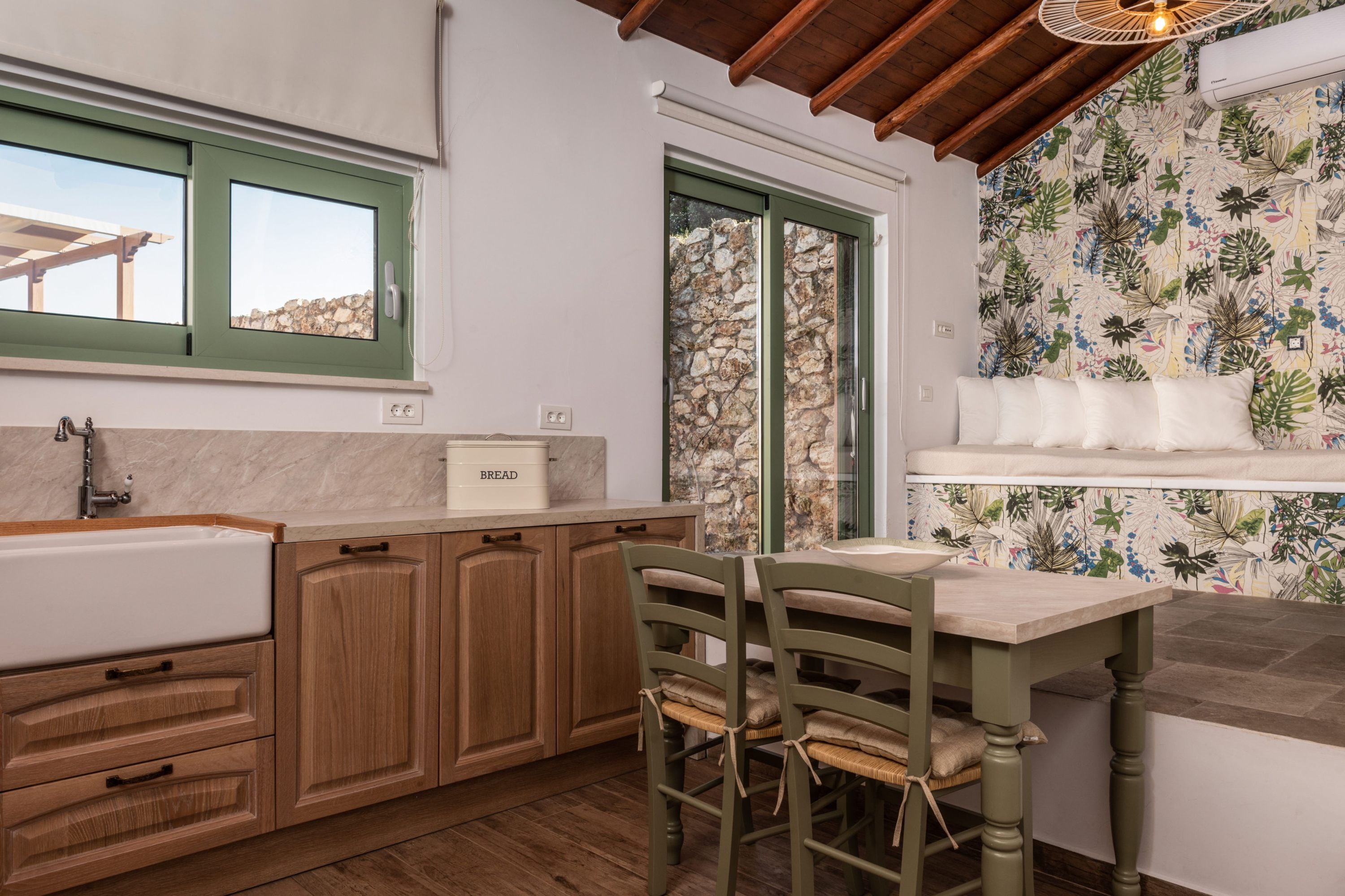Una cocina con armarios de madera, un lavamanos, una ventana con vistas, una mesa con sillas y una pared con un diseño de hojas.