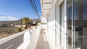 A balcony with a view of a hilly landscape, a palm tree, and a distant power line. - Oasis Tenerife Apartamento (Granadilla de Abona)