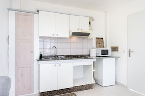 Una cocina compacta con armarios blancos, un microondas y un refrigerador pequeño.
