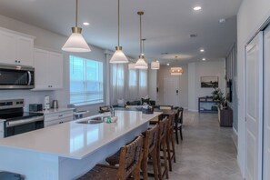 A modern kitchen with a large island, stainless steel appliances, pendant lighting, and a view to the dining area. - 5BR Home with Private Pool at Windsor Cay (Clermont)