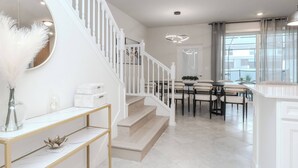 Une cuisine moderne avec des meubles blancs, un coin repas doté d’une table ronde et un escalier avec des rampes blanches.