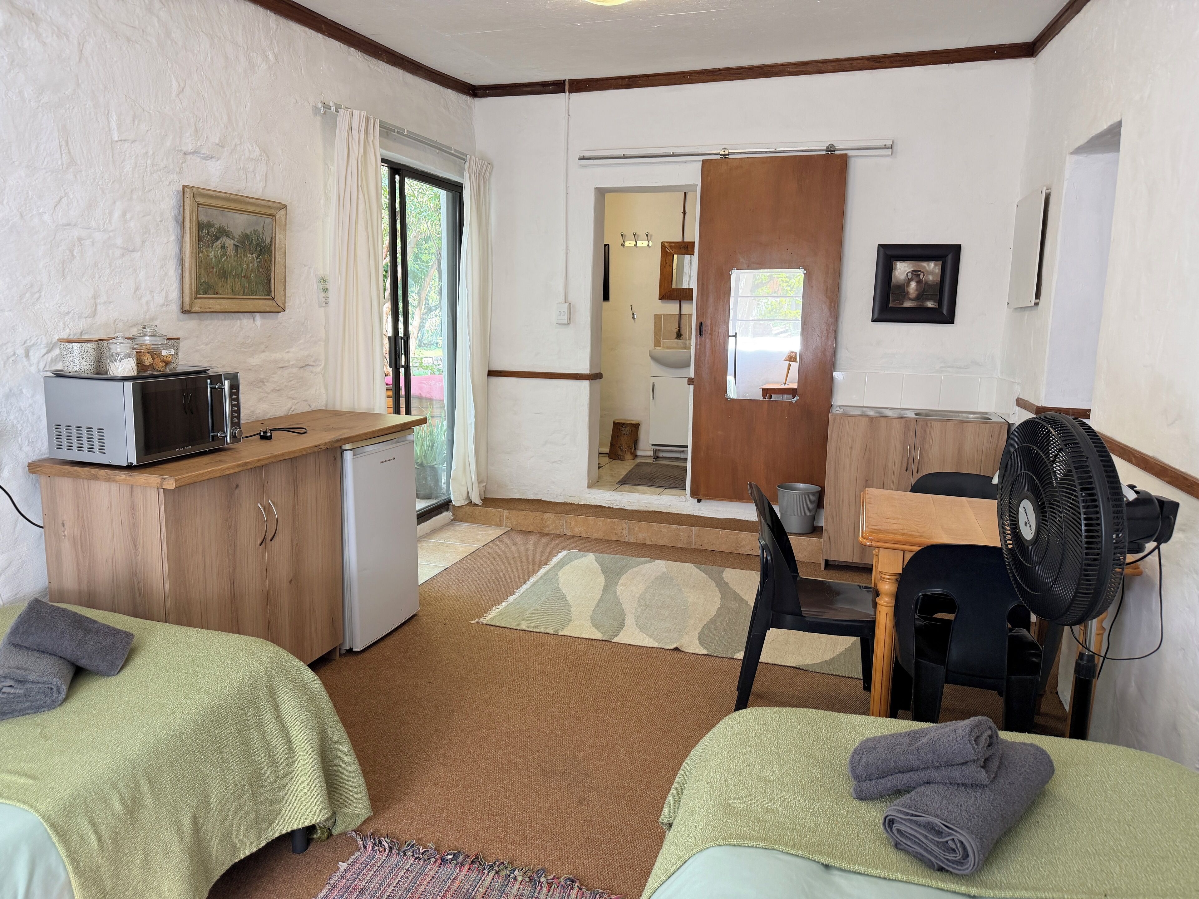 Une petite pièce propre, avec deux lits, un coin cuisine, un espace repas et une salle de bain visible à travers une porte ouverte.