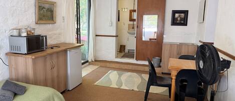 Une petite pièce propre, avec deux lits, un coin cuisine, un espace repas et une salle de bain visible à travers une porte ouverte.