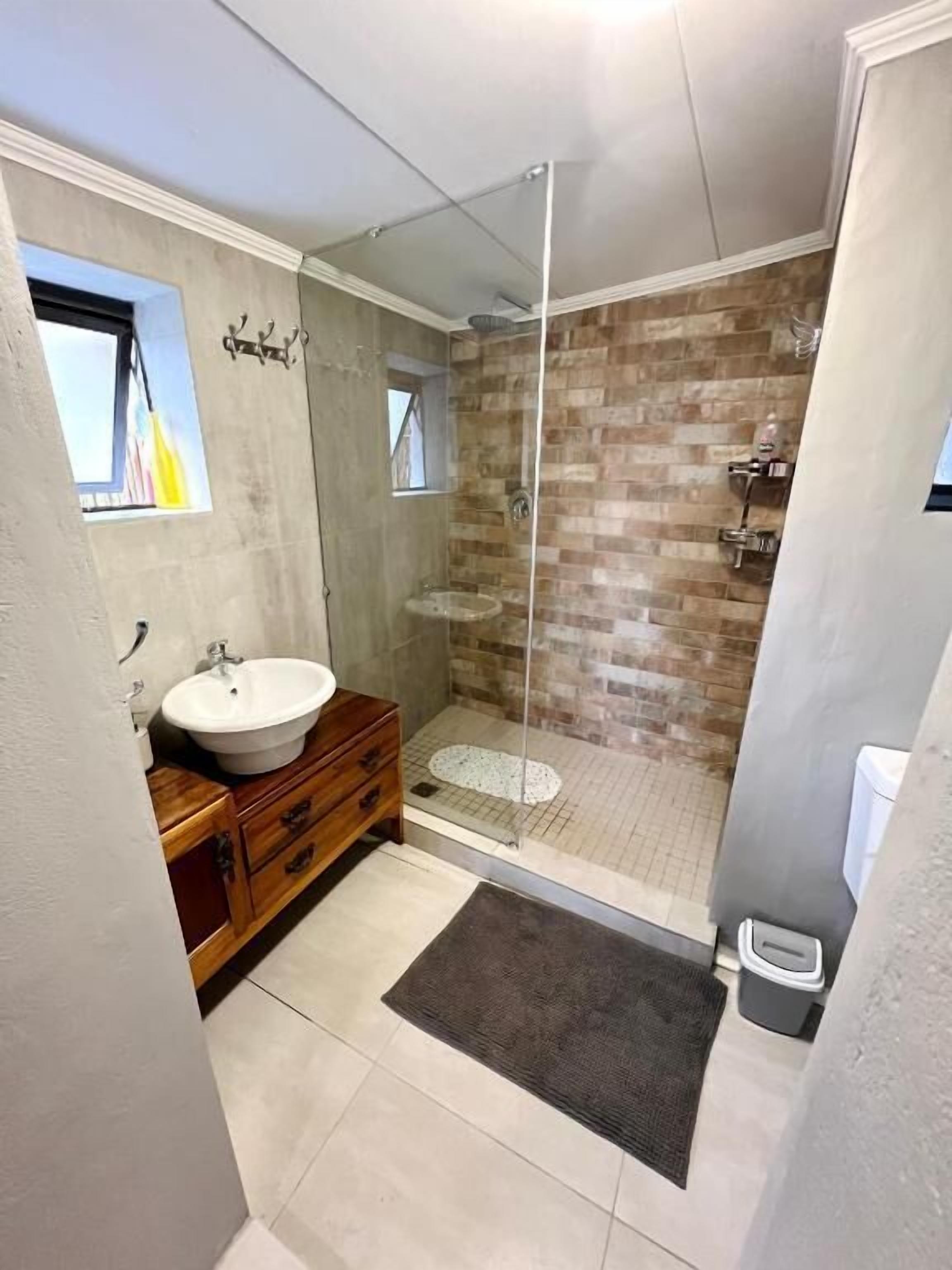 A modern bathroom with a glass-enclosed shower, a wooden vanity, and a small window.