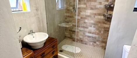 A modern bathroom with a glass-enclosed shower, a wooden vanity, and a small window.