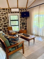 A cozy living room with a stone wall, a television mounted above a window, a wooden sofa, and a coffee table.
