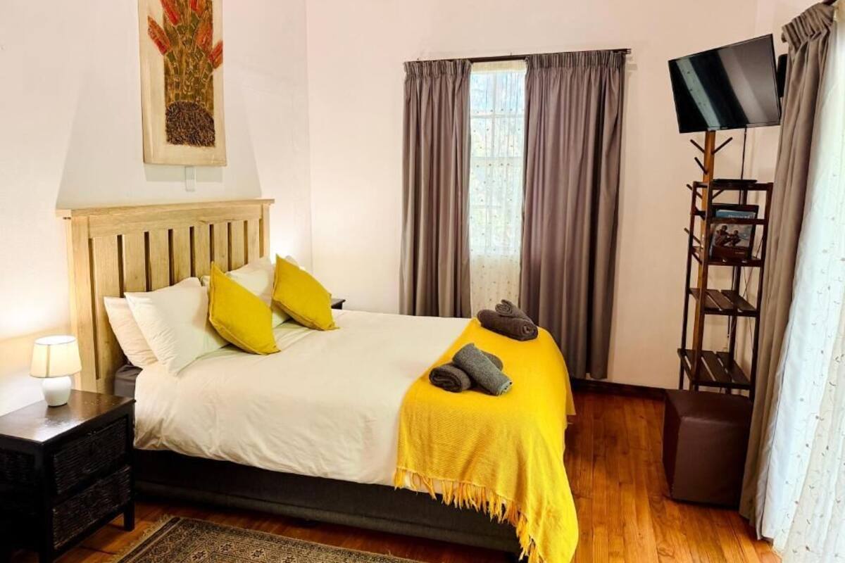 Un lit bien fait, agrémenté d’un plaid jaune, une lampe de chevet et un tableau au mur.