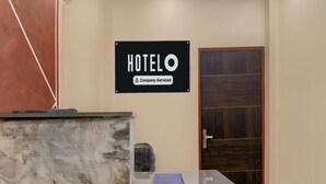 A reception desk with a sign that reads "HOTELO Company-Serviced" and a wooden door in the background. - Hotel O Singar Nagar Metro Station (Lucknow)