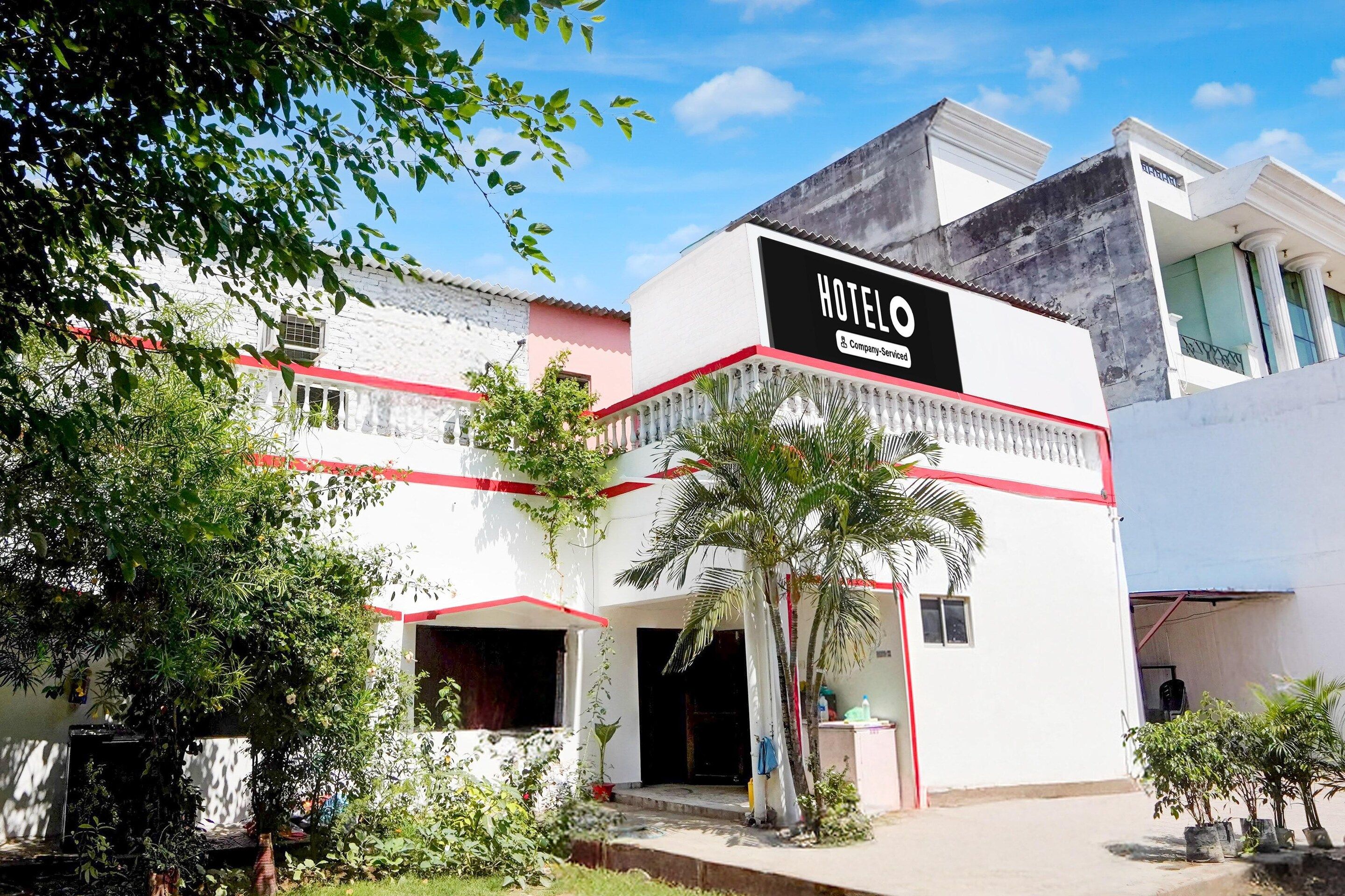 A hotel with a prominent sign, a red and white facade, and a small garden area with palm trees.