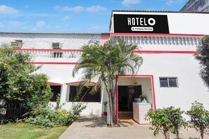 Un hôtel appelé « HOTELO », doté d’une enseigne fournie par l’entreprise, d’une façade blanche et de bordures rouges. On y trouve des plantes en pot et un ciel dégagé.