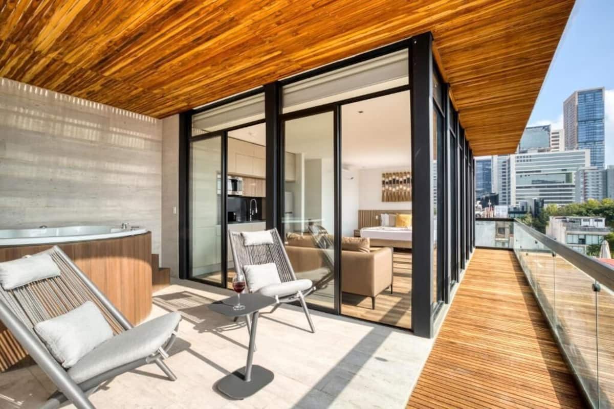 A modern rooftop terrace with a wooden ceiling, a glass-enclosed kitchen, and a seating area with a table and chairs.