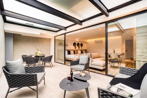 Ein modernes Wohnzimmer mit Glastrennwand, Rattanmöbeln und einem kleinen runden Tisch mit einem Glas Rotwein.