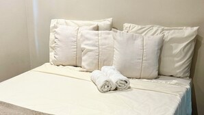 Ein ordentlich bezogenes Bett mit weißen Leinen und Kissen, ein gefaltetes Handtuch und eine beige Tagesdecke.