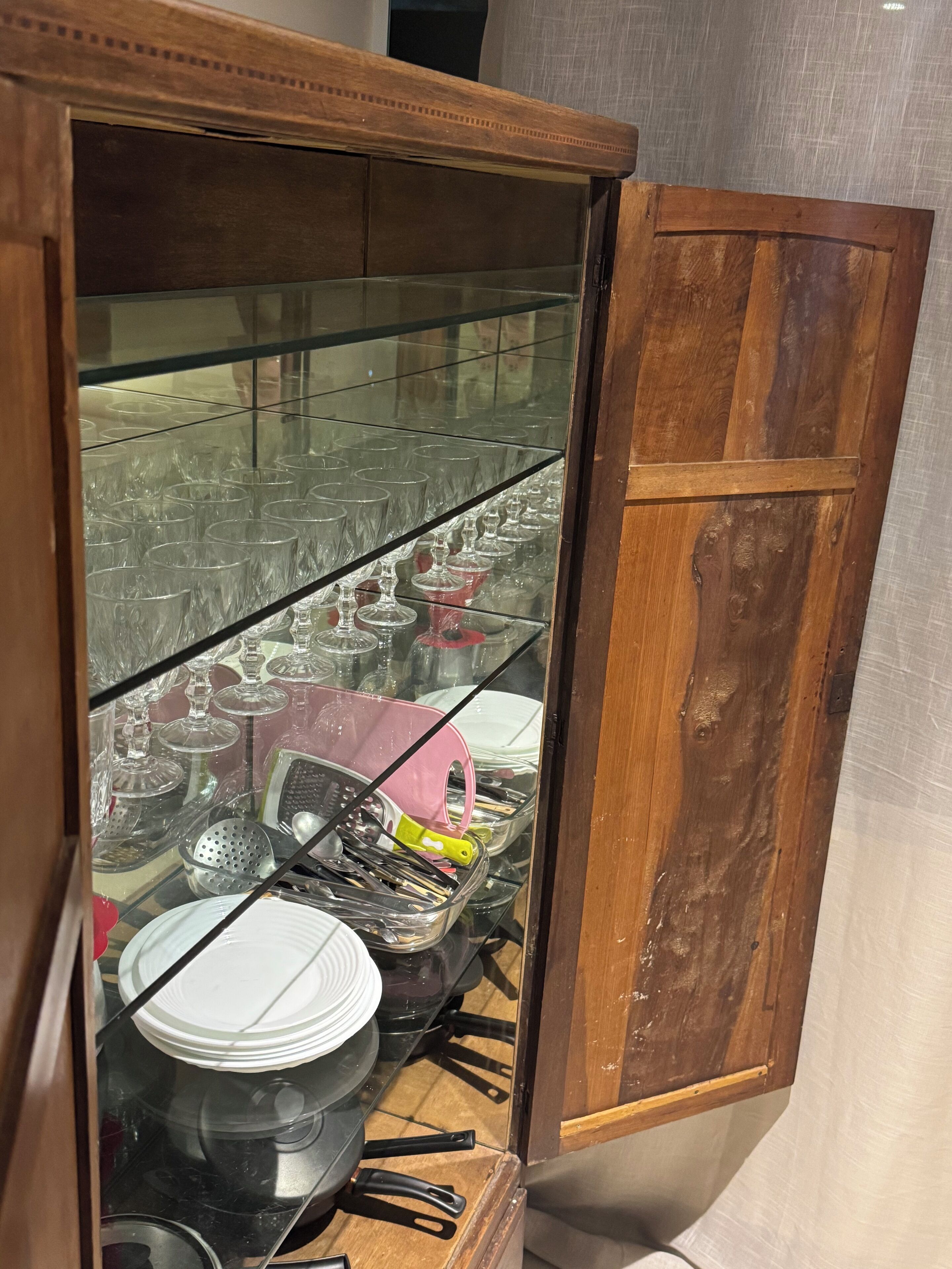Un meuble en bois doté de portes en verre, renfermant divers ustensiles de cuisine, tels que des assiettes, des bols et des couverts.