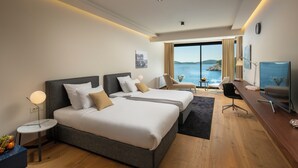 Ett modernt hotellrum med två sängar, ett skrivbord, en stol och ett stort fönster med utsikt över havet.
