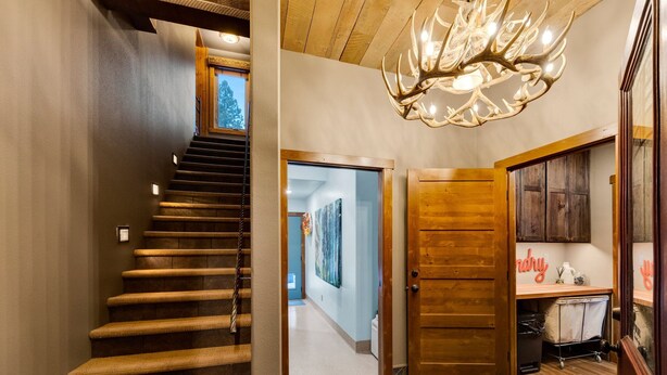 Una escalera conduce a un segundo piso, una puerta de madera, un pasillo con obras de arte y un candelabro.