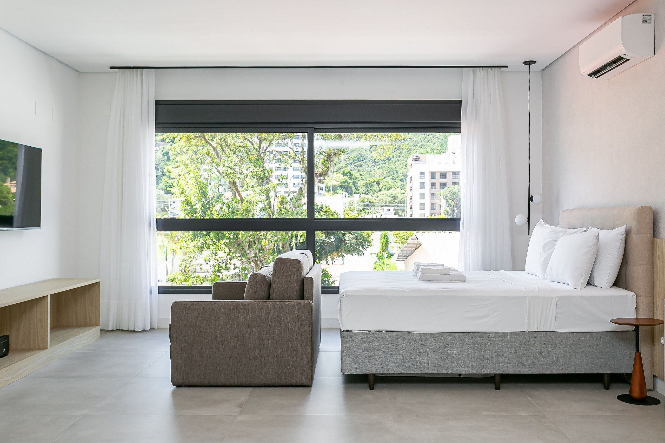 Une chambre d’hôtel moderne avec un grand lit, un canapé, une télévision et une fenêtre donnant sur la ville.