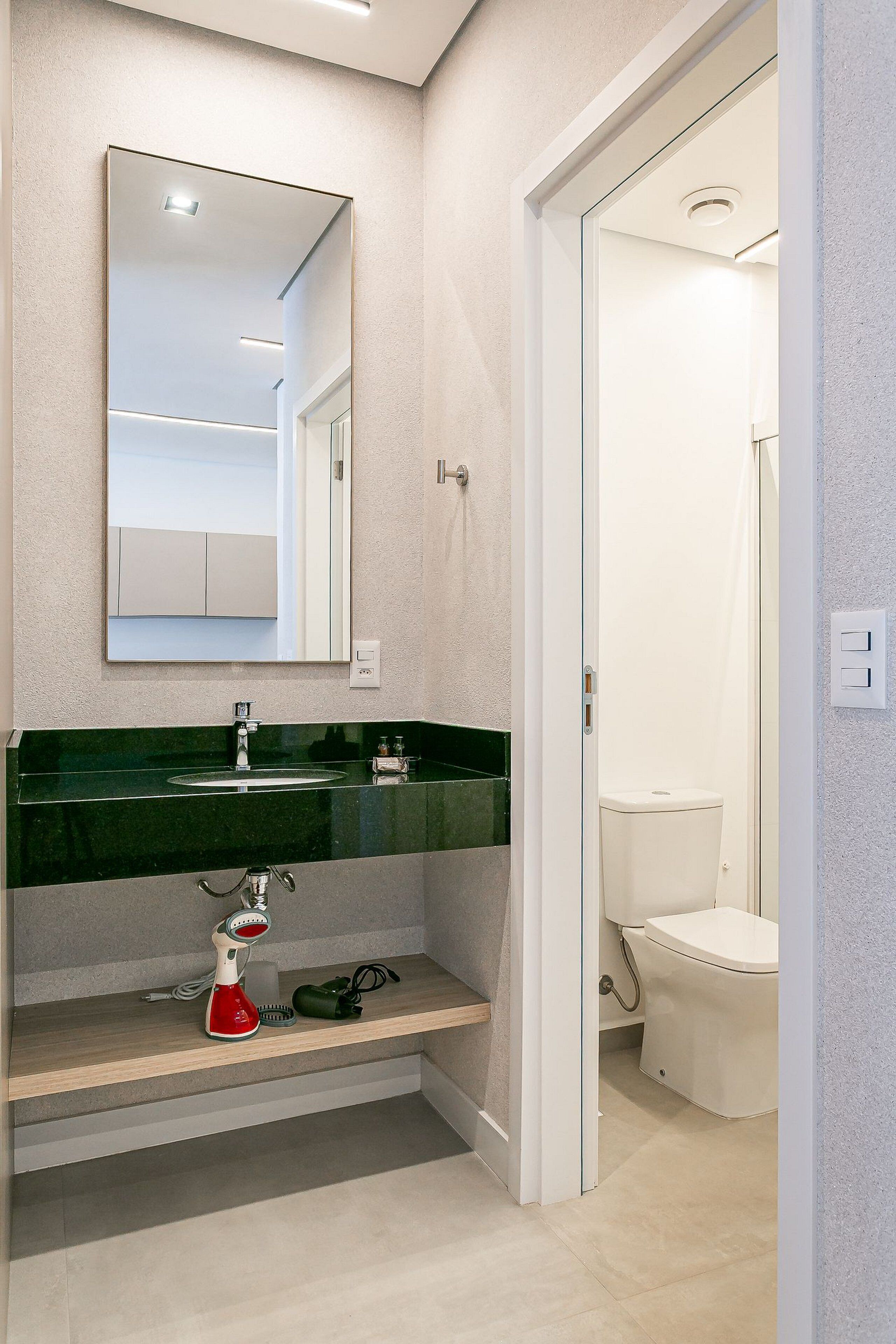 A modern bathroom with a green sink, a mirror, and a toilet.