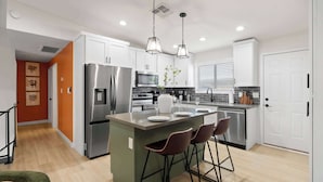 A modern kitchen with white cabinets, stainless steel appliances, and a central island with bar stools. - Piece of Paradise • Pool, Games, Fire Pit, Hot tub (Glendale)