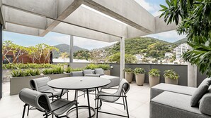 A modern outdoor patio with a round table and chairs, a grey sofa, and potted plants. - Modern studio | Near Technology Hub | Gym #SG06 (Florianópolis)