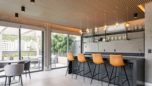 A modern bar area with a high ceiling, large windows, and a view of buildings and greenery. - Modern studio | Near Technology Hub | Gym #SG06 (Florianópolis)