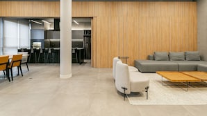 A modern interior with a grey sofa, wooden panel walls, and a dining area with chairs and tables. - Modern studio | Near Technology Hub | Gym #SG06 (Florianópolis)