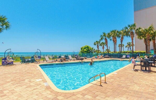 A pool area with lounge chairs and palm trees, overlooking the ocean.
