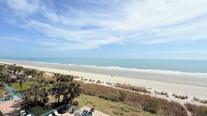 A beach view with a clear sky, a sandy beach, and some vegetation. - Beautiful Oceanfront Studio, pool (Myrtle Beach)