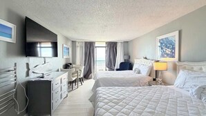 A hotel room with two beds, a desk, a TV, and a balcony with curtains. - Beautiful Oceanfront Studio, pool (Myrtle Beach)