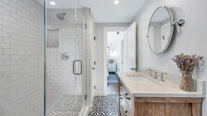 Une salle de bain moderne dotée d’une douche à parois de verre, d’un grand miroir et d’un meuble-lavabo avec un évier et un placard.