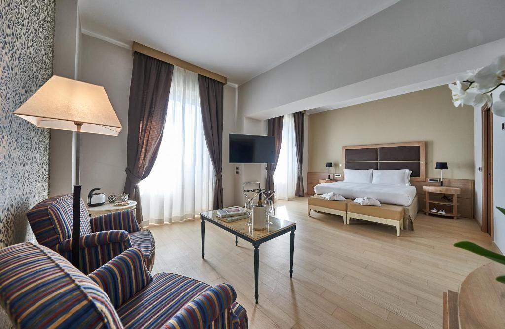 Una habitación de hotel con cama, sofá, mesa de centro, televisor y lámpara.