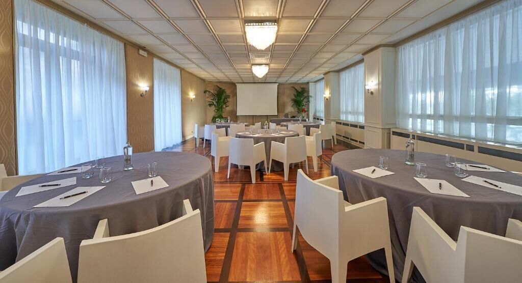 Een congreszaal met ronde tafels, witte stoelen en een groot scherm aan de voorkant.