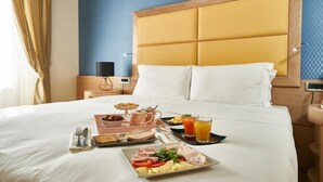 A hotel room with a neatly made bed, breakfast tray with eggs, toast, and juice, and a bedside table with a lamp. - Hotel Astoria (Biella)