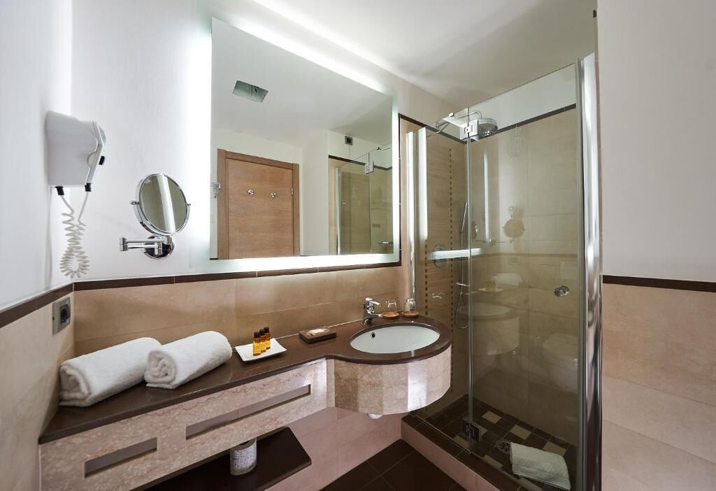 Un baño moderno con ducha envuelta en vidrio, tocador con lavamanos y un secador de pelo montado en la pared.