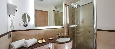 Un baño moderno con ducha envuelta en vidrio, tocador con lavamanos y un secador de pelo montado en la pared.