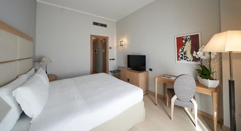 Una habitación de hotel con una cama grande, un escritorio con silla, televisión y una lámpara de escritorio.