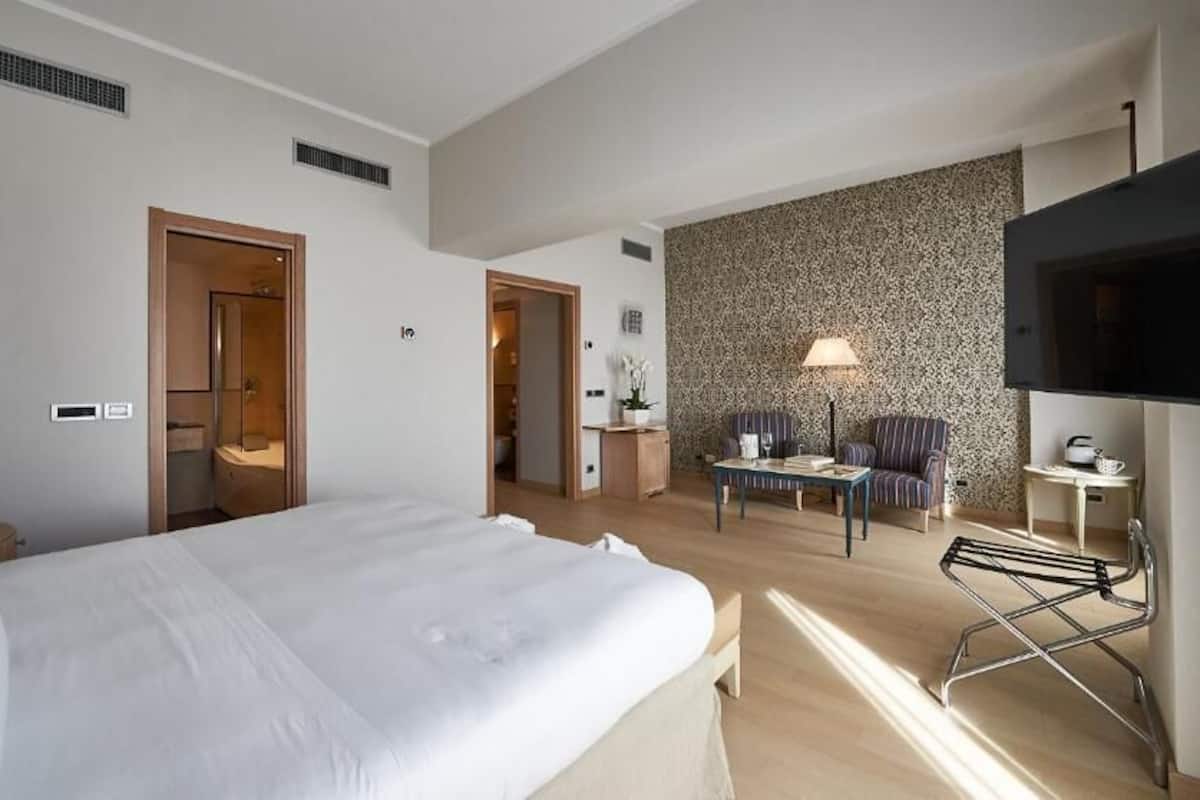 A hotel room with a large bed, a desk with a chair, a television, and a patterned wall.