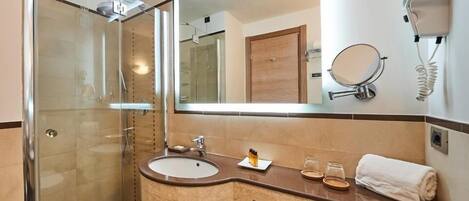 Un baño moderno con cabina de ducha de vidrio, un lavabo con tocador, un espejo y un secador de pelo montado en la pared.