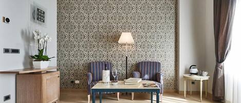 A room with a patterned wallpaper, a table with chairs, a lamp, a small side table, and a cabinet.