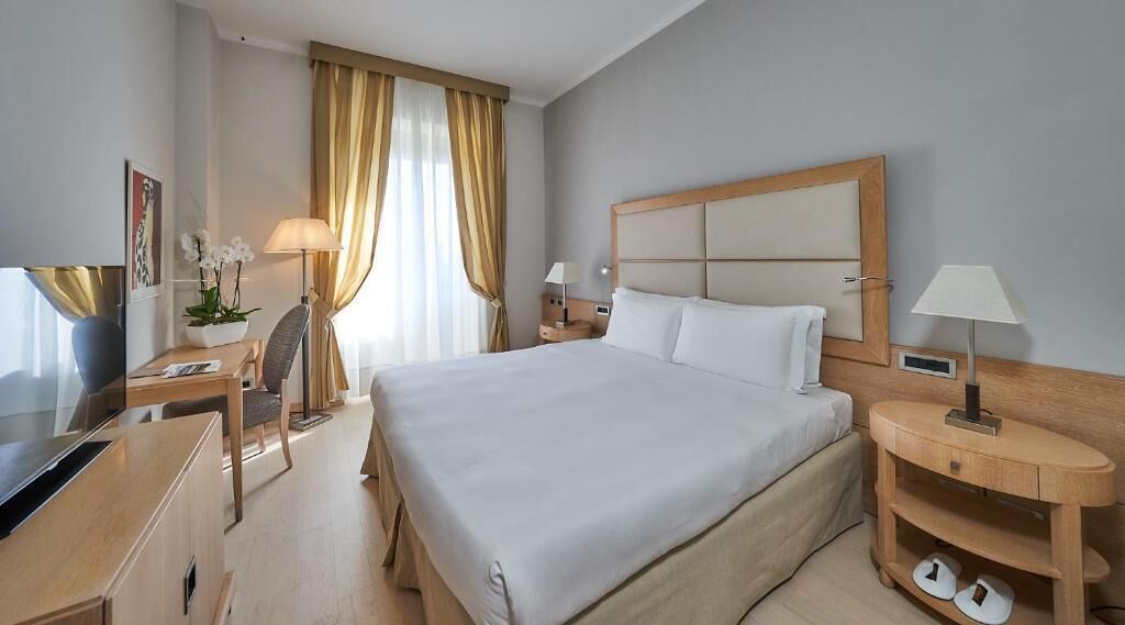 Une chambre d’hôtel avec un grand lit, un bureau avec une chaise, une télévision et une lampe.