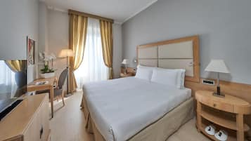 Ein Hotelzimmer mit einem großen Bett, einem Schreibtisch mit Stuhl, einem Fernseher und einer Lampe.