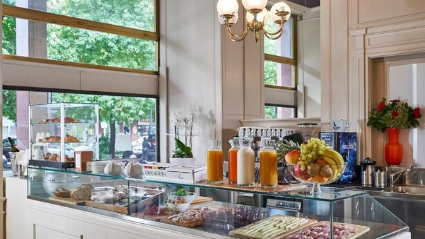 A breakfast buffet with various food items and beverages, a glass display case, and a chandelier. - Hotel Astoria (Biella)