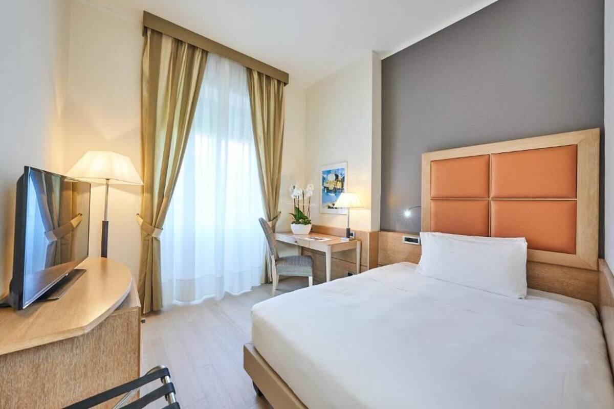 A hotel room with a bed, desk, chair, TV, and curtains.